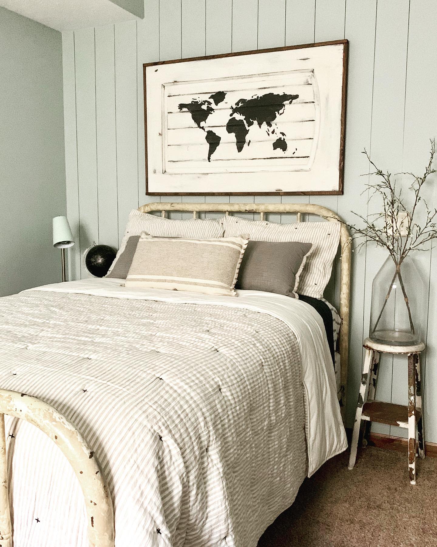 Rustic bedroom with world map wall art, neutral bedding, and distressed wood furniture.